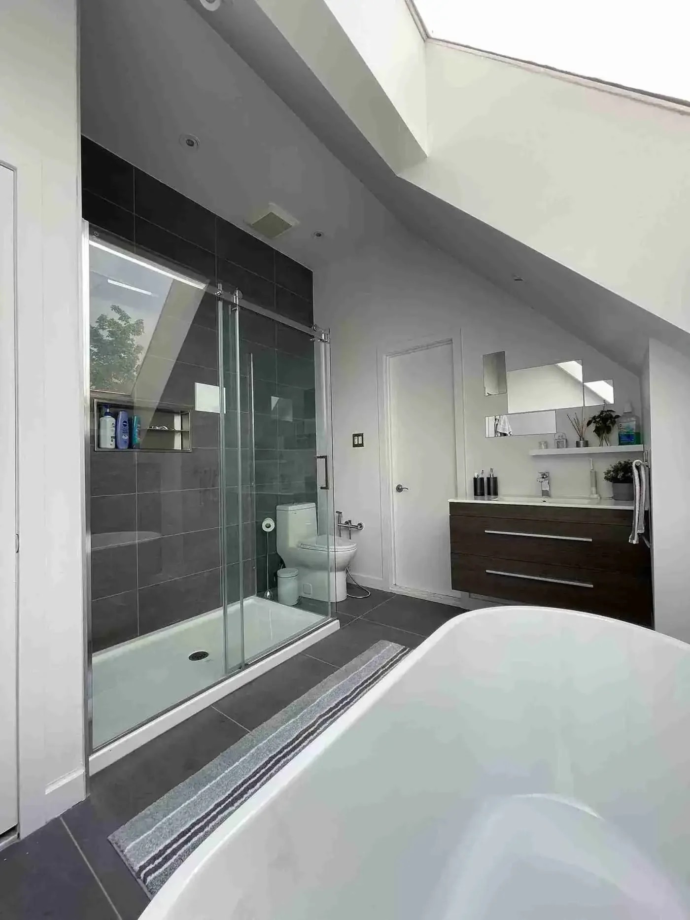 Sloped-ceiling bathroom with dark tile shower and floating vanity