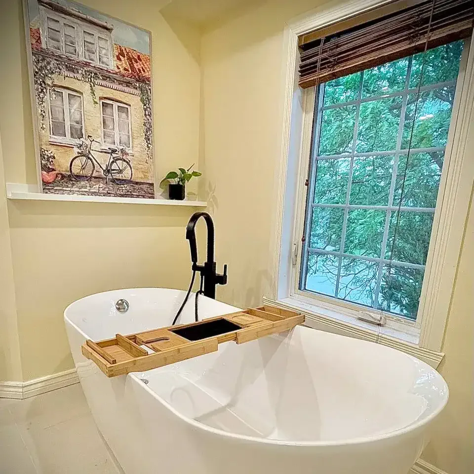 Freestanding tub with black floor-mounted faucet beside a bright window