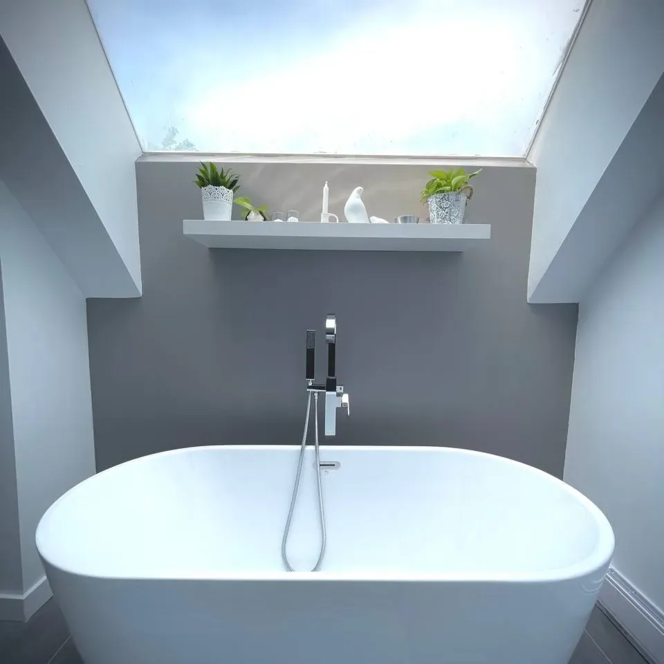 Oval freestanding tub against a grey feature wall below a skylight