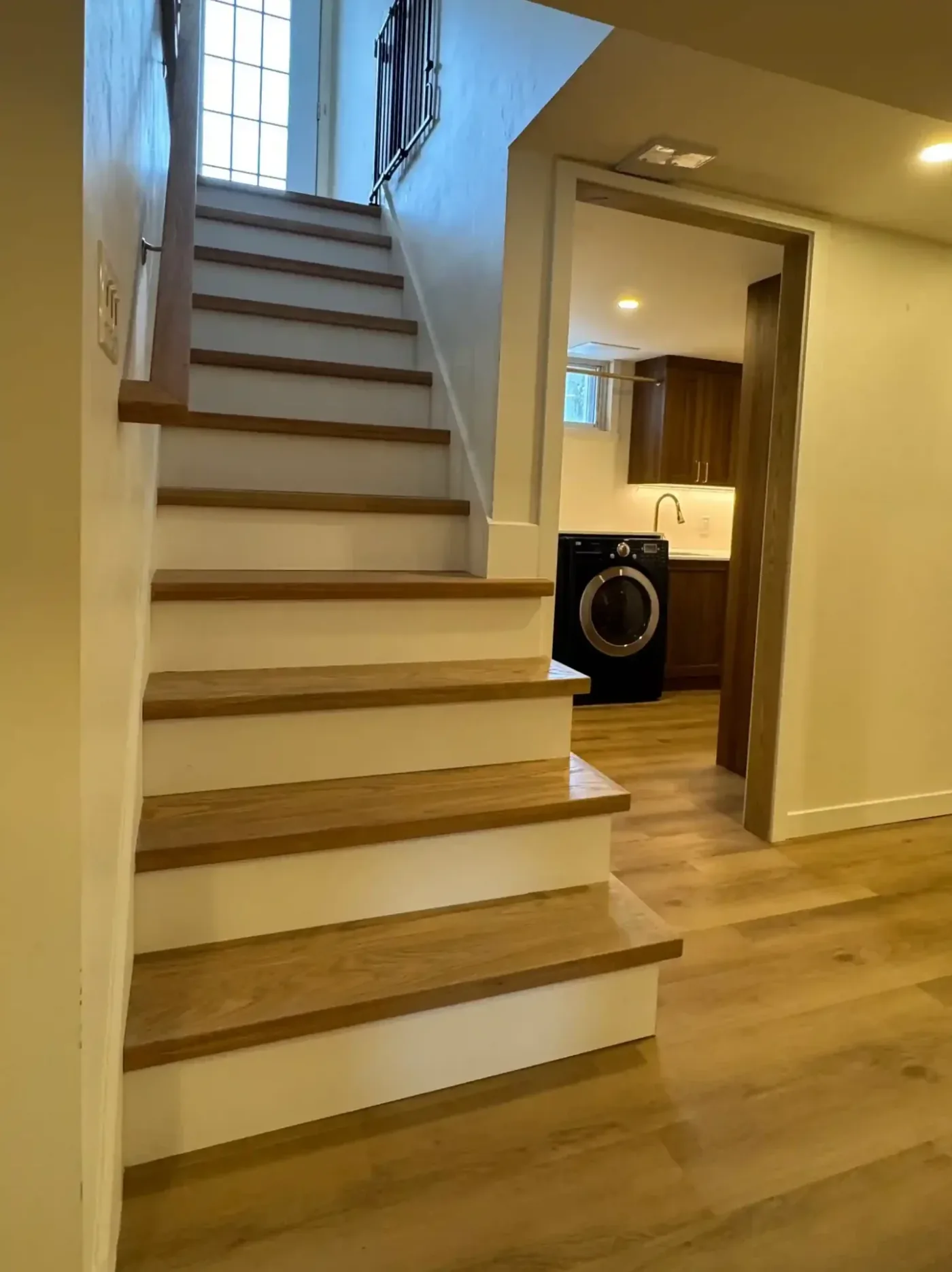 Oak staircase with white risers leading to a renovated laundry room